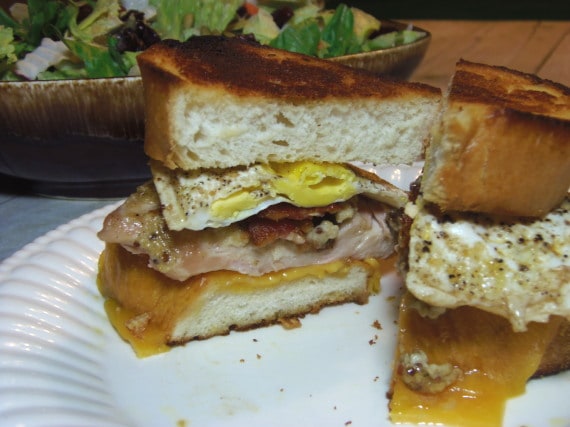 A Chicken and Egg Sandwich on a white plate with melted cheese and bacon.