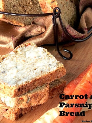 Slices of buttered Carrot and Parsnip Bread on a cutting board with carrots and parsnips on the side.