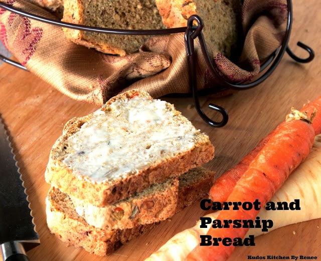 Slices of buttered Carrot and Parsnip Bread on a cutting board with carrots and parsnips on the side.