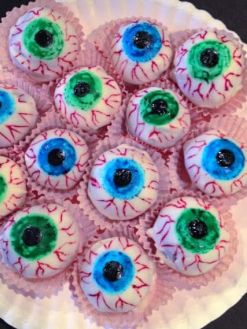 A paper plate filled with Eye Candy Cake Balls on a black background.