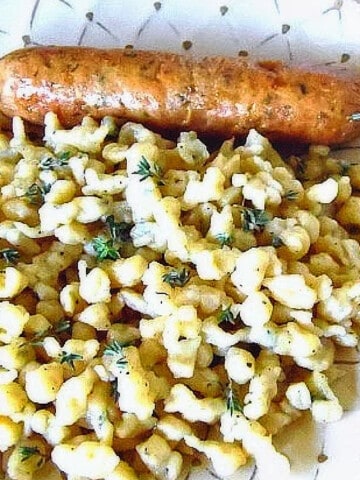 Spaetzle with Thyme on a plate with a sausage.