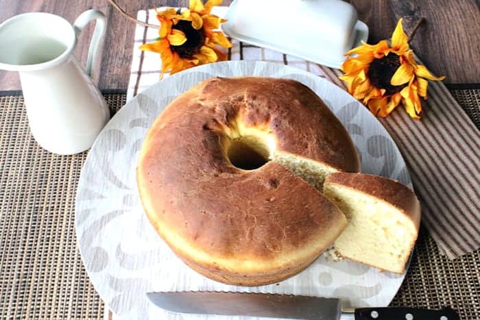 A round loaf of Sally Lunn bread with a slice taken out with sunflowers in the background.