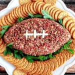 An overhead photo of a Football-Shaped Cheeseball with Pecans, crackers, and parsley on a platter.
