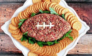 An overhead photo of a Football-Shaped Cheeseball with Pecans, crackers, and parsley on a platter.