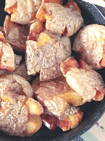 A bunch of crispy golden Fried Smashed Potatoes in a cast iron skillet.