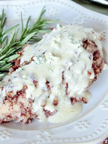 A breast of Pecan Chicken with Blue Cheese Sauce on a white plate with a sprig of rosemary.