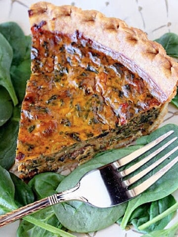 A slice of Pumpkin and Spinach Quiche on a plate with fresh spinach and a fork.