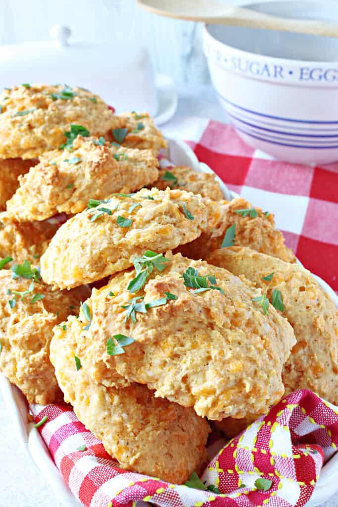 A vertical closeup of Better Cheddar Bay Biscuits along with a red and white checked napkin, and fresh parsley on top.