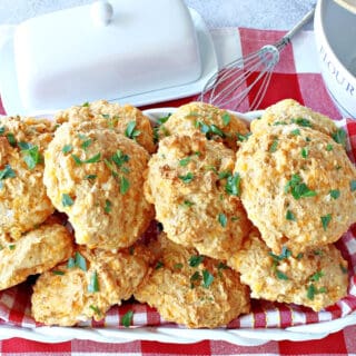 A white basket with a red and white checked napkin filled with Cheddar Bay Biscuits.