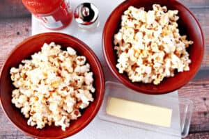 An overhead photo of two bowls filled with Buffalo Popcorn and a butter dish with butter.