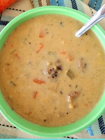 A serving of Beer Cheese Soup with Bratwurst in a green bowl with a spoon.