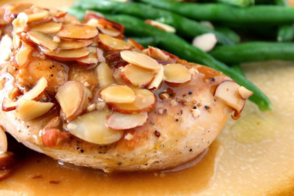 Closeup photo of a chicken beer bake breast with almonds and green beans in the background.