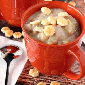 A red mug filled with Clam and Shrimp Chowder and topped with oyster crackers.