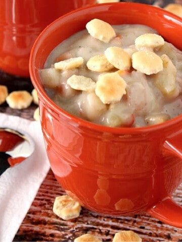 A red mug filled with Clam and Shrimp Chowder and topped with oyster crackers.
