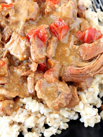 A serving of Gingered Pork with Orange Sauce over brown rice on a black plate.