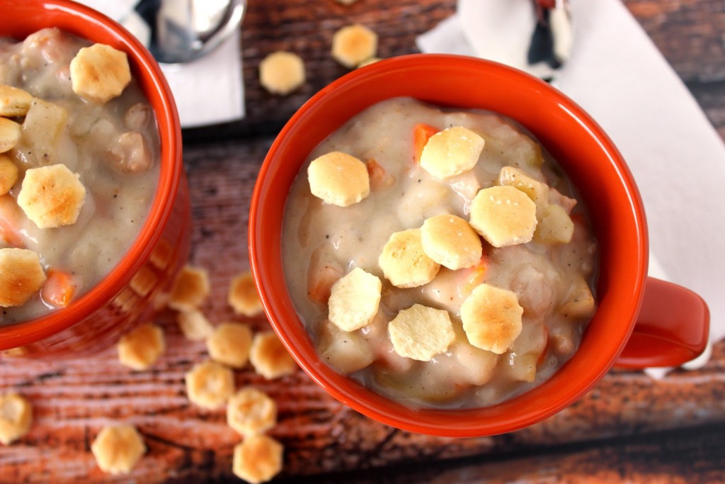 An overhead photo of two orange mugs filled with Clam and Shrimp Chowder with oyster crackers on the top.