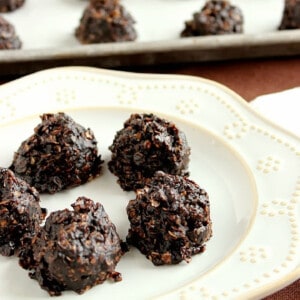 A white plate filled with 5 No Bake Chocolate Peanut Butter Cookies with a baking sheet in the background.