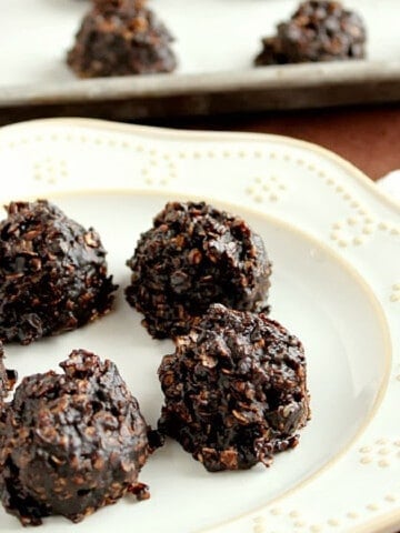 A white plate filled with 5 No Bake Chocolate Peanut Butter Cookies with a baking sheet in the background.