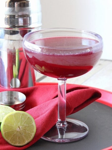 A Mixed Berry Margarita on a red serving tray with a lime and cocktail shaker.