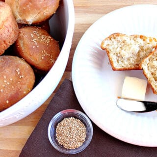 An overhead photo of a Sesame Seed Dinner Roll on a plate with a pat of butter and a butter knife on the side.