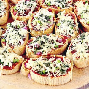 A bunch of Mini French Bread Pizza Appetizers topped with cheese and basil leaves.