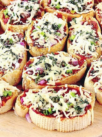 A bunch of Mini French Bread Pizza Appetizers topped with cheese and basil leaves.