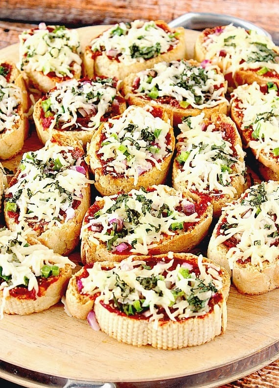 Mini French Bread Appetizer Pizzas Mini French Bread Appetizer Pizzas with cheese and basil on a wooden cutting board.