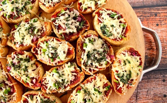 Mini French Bread Appetizer Pizzas on a wooden cutting board.