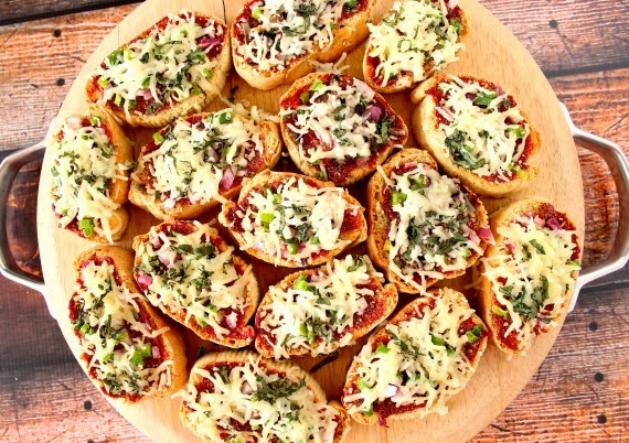 A round wooden cutting board filled with mini French bread pizza appetizers.