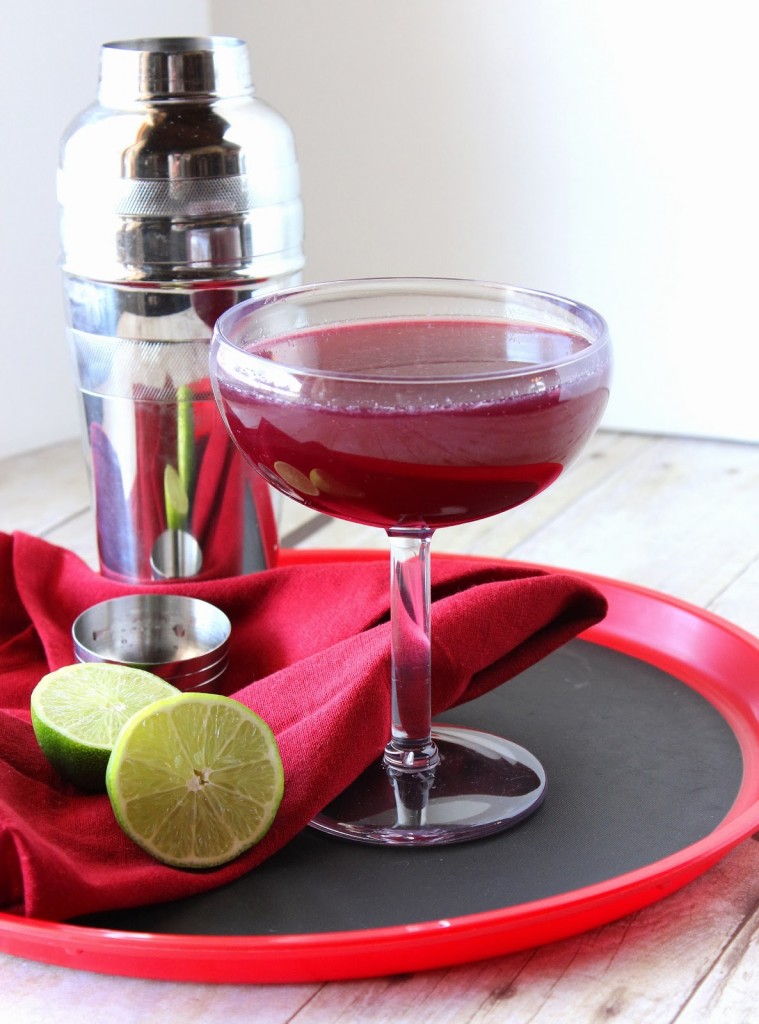 A Mixed Berry Margarita on a red serving tray with a lime and cocktail shaker.