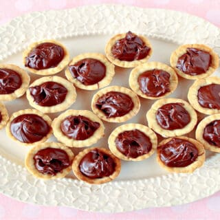 A direct overhead horizontal photo of Nutella Cookie Cups on a pretty white platter with a pink and white polka dot tablecloth.