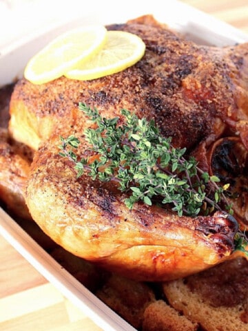 A whole Basic Roast Chicken with lemon slices and fresh thyme.