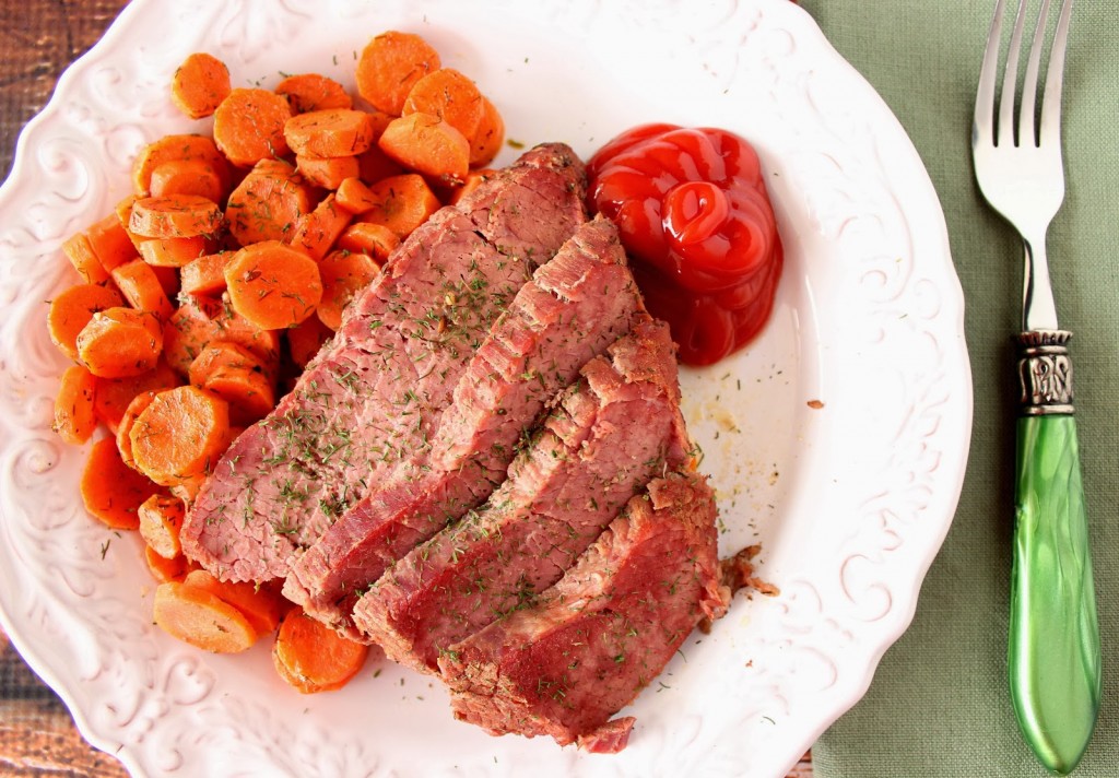 A serving of Slow Cooker Corned Beef and Carrots on a white plate with dill.