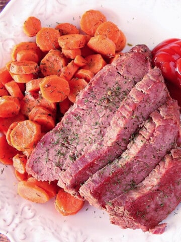 A serving of Slow Cooker Corned Beef and Carrots on a white plate with dill.