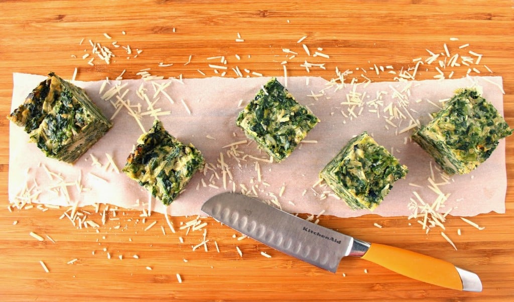 Overhead picture of 5 spinach artichoke crustless quiche squares on a cutting board with a knife.