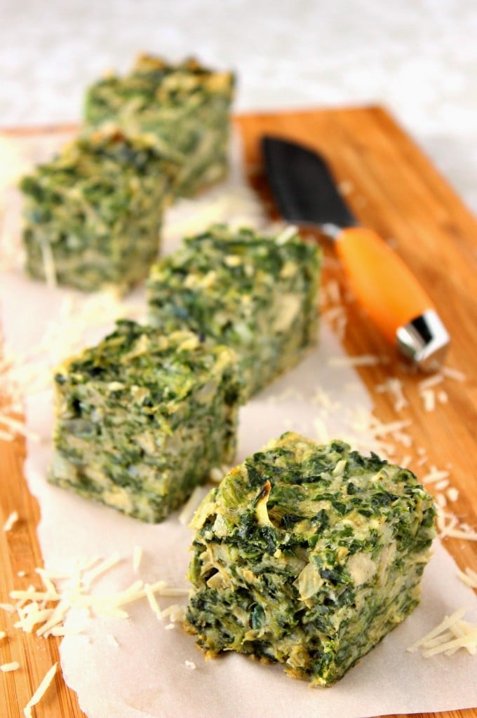 Vertical photo of spinach squares on a cutting board with white parchment paper and a knife.