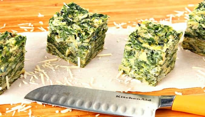 Square of Artichoke and Spinach on a wooden cutting board with shredded Parmesan cheese and a knife. bbq side dish recipes roundup