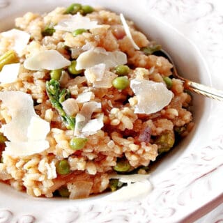 An offset horizontal photo of a pretty white bowl filled with Asparagus and Pea Risotto with Parmesan cheese shavings on top.