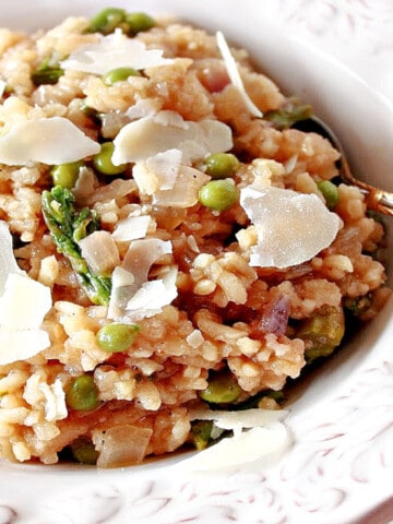 An offset horizontal photo of a pretty white bowl filled with Asparagus and Pea Risotto with Parmesan cheese shavings on top.