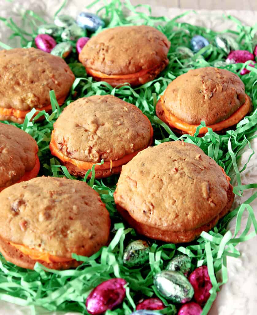 A closeup vertical image of Carrot Cake Whoopie Pies on a platter surrounded by green Easter grass.