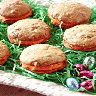 A white platter filled with green Easter grass and Carrot Cake Whoopie Pies.