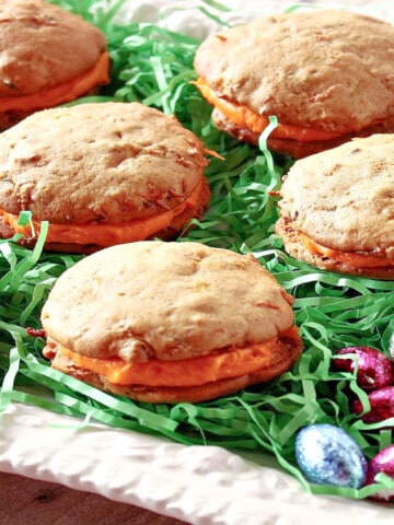 A white platter filled with green Easter grass and Carrot Cake Whoopie Pies.