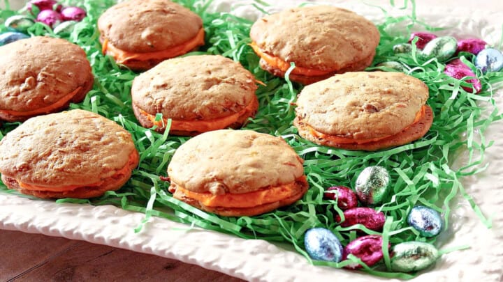 A white platter filled with green Easter grass and Carrot Cake Whoopie Pies.