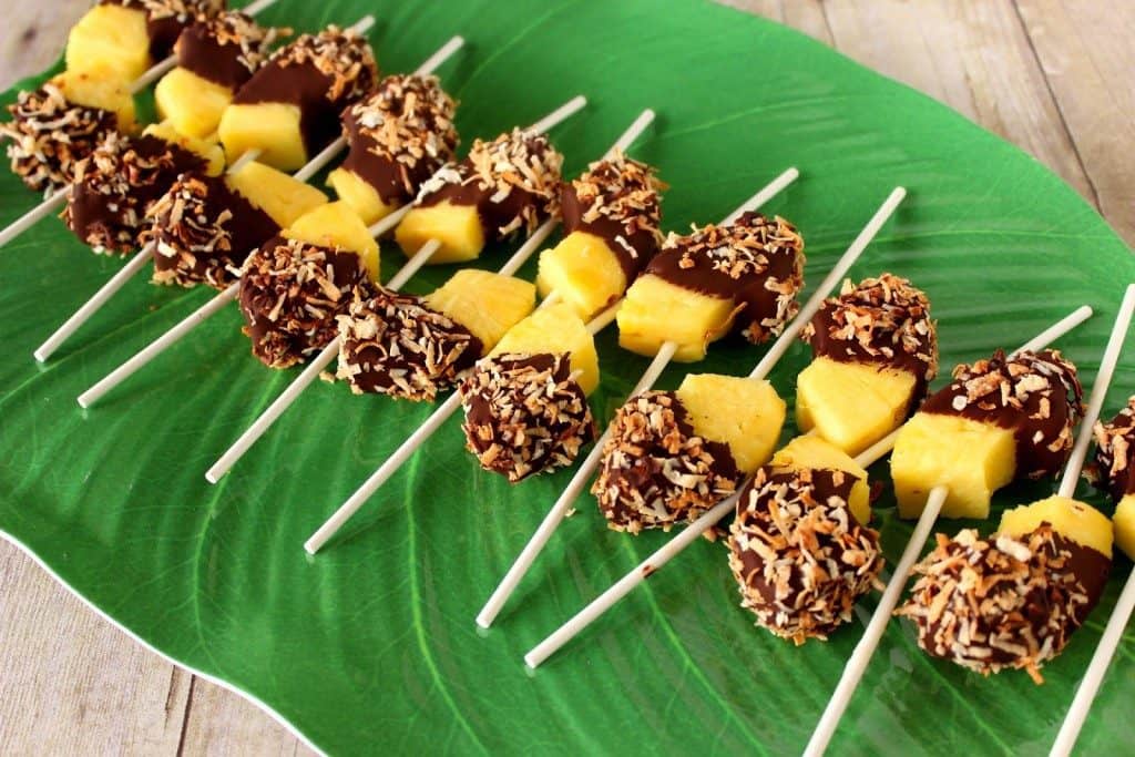Green leaf platter lined up with frozen pineapple pops with chocolate and toasted coconut.
