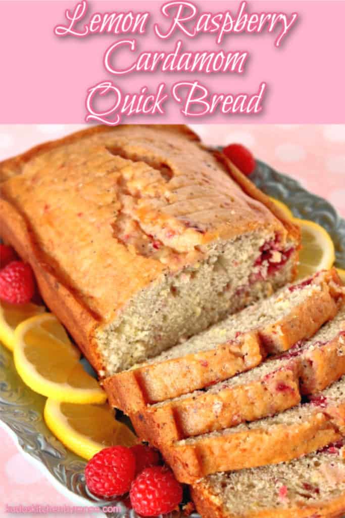 A closeup photo of a sliced loaf of lemon raspberry cardamom quick bread on a blue plate with lemon slices and raspberries.