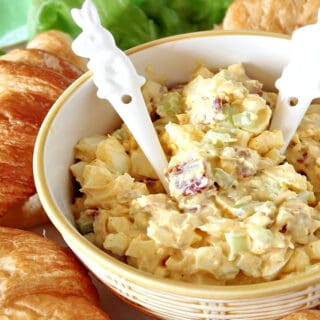 A bowl of Bacon Egg Salad with two bunny spoons surrounded by croissants.