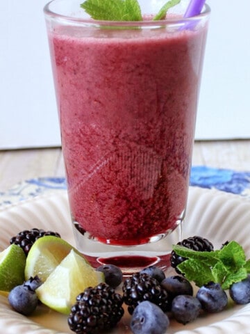A glass of Blackberry Smoothie along with fresh mint on a plate.