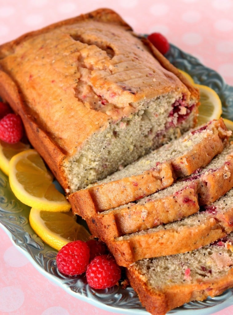 A vertical closeup image of lemon raspberry quick bread with lemon slices and fresh raspberries.