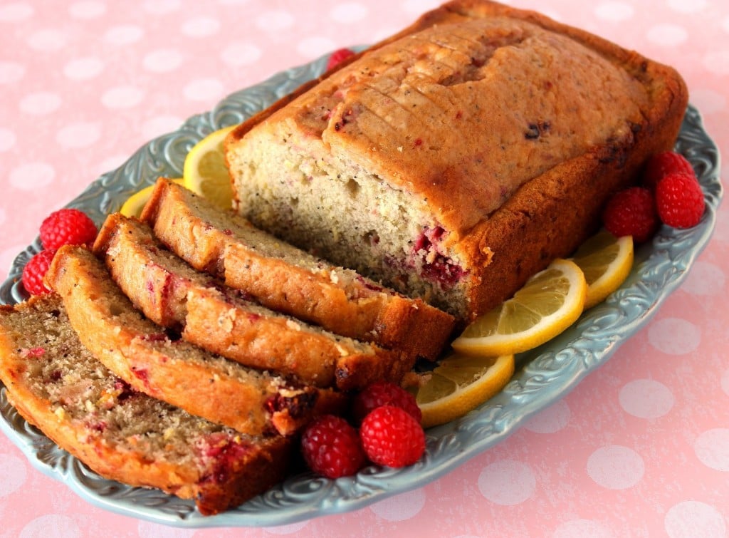 A loaf of lemon raspberry cardamom quick bread on a pretty blue plate on a pink polka dot table cloth.