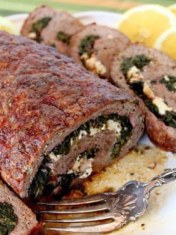 A Rolled Greek Meatloaf stuffed with spinach and feta cheese on a platter with a serving fork.